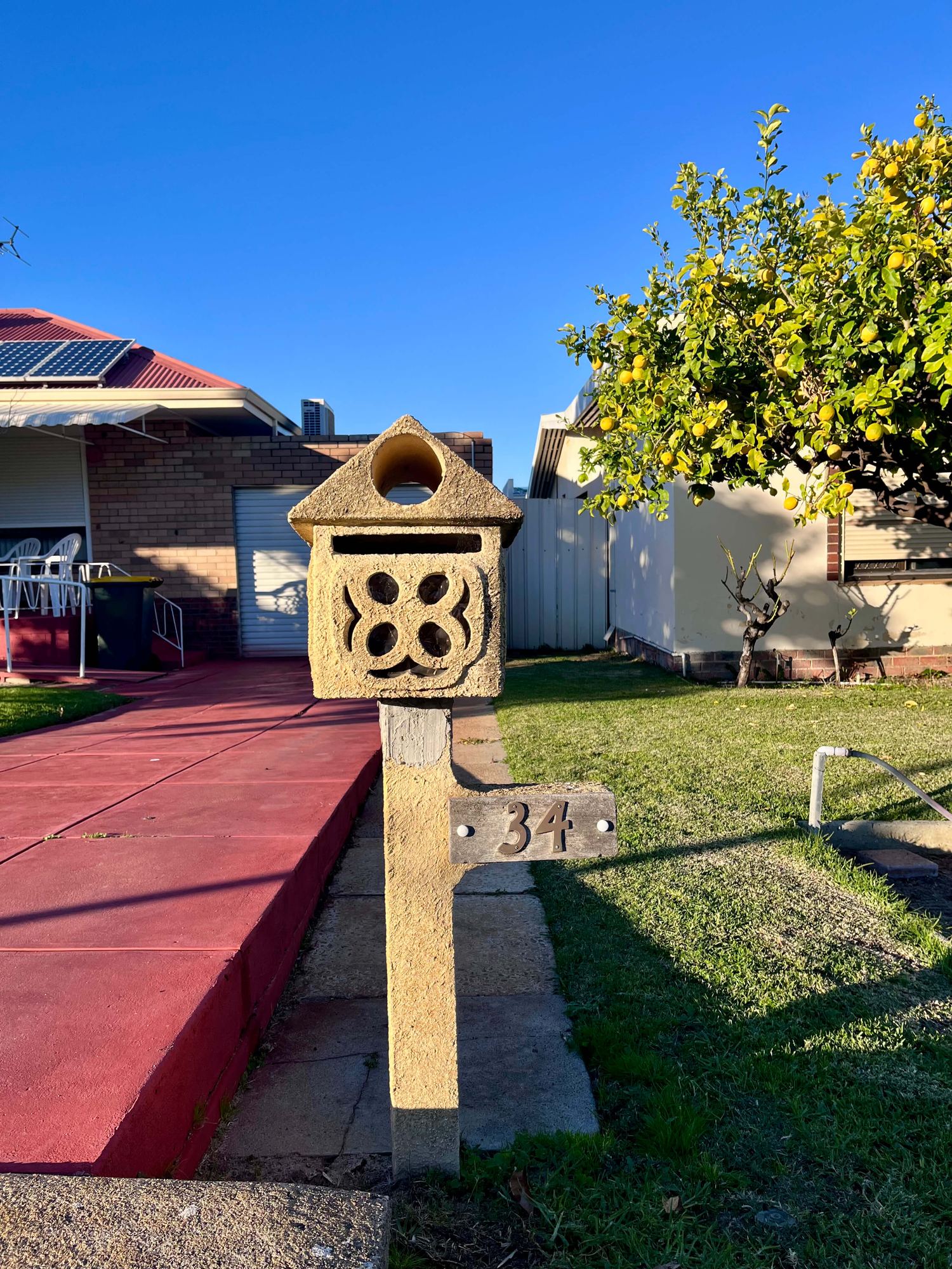 A textured cream letterbox shaped like a little house, numbered 34, beside a lemon tree heavy with fruit