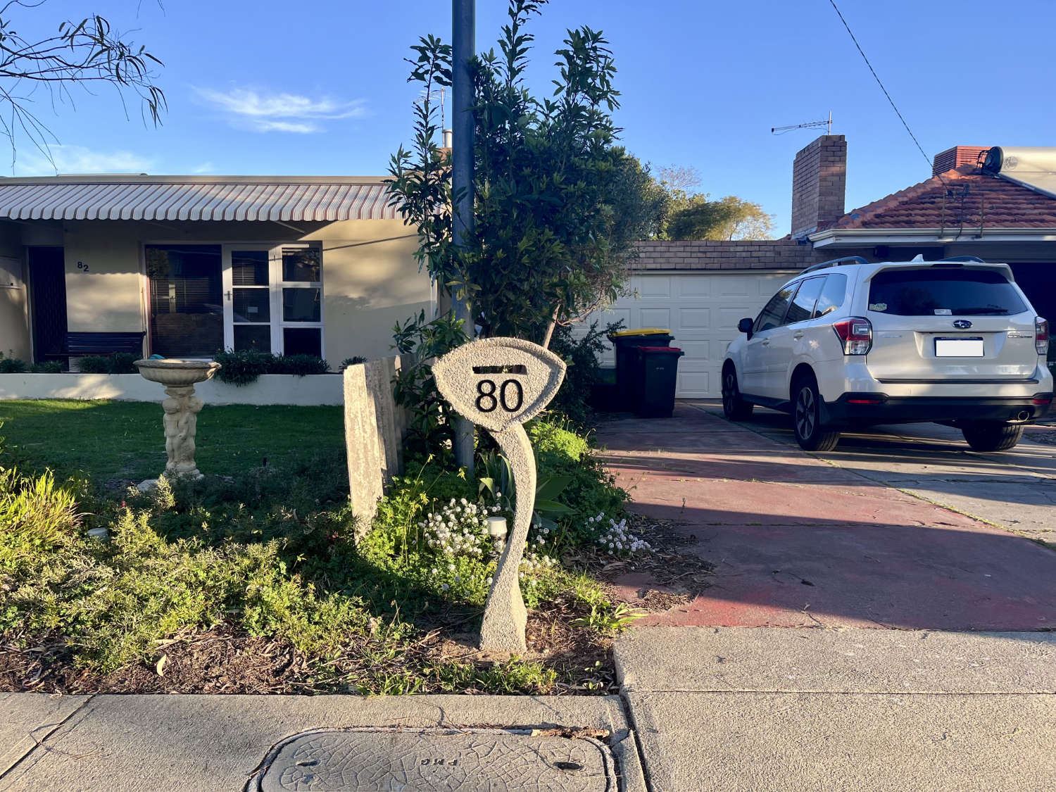 A carved stone letterbox numbered 80, standing beside a concrete birdbath on the front lawn