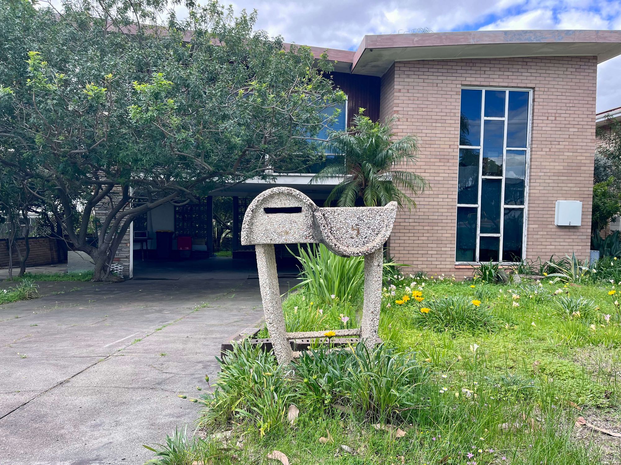 A pale, pebble-textured letterbox with a scalloped roof and curved concrete legs